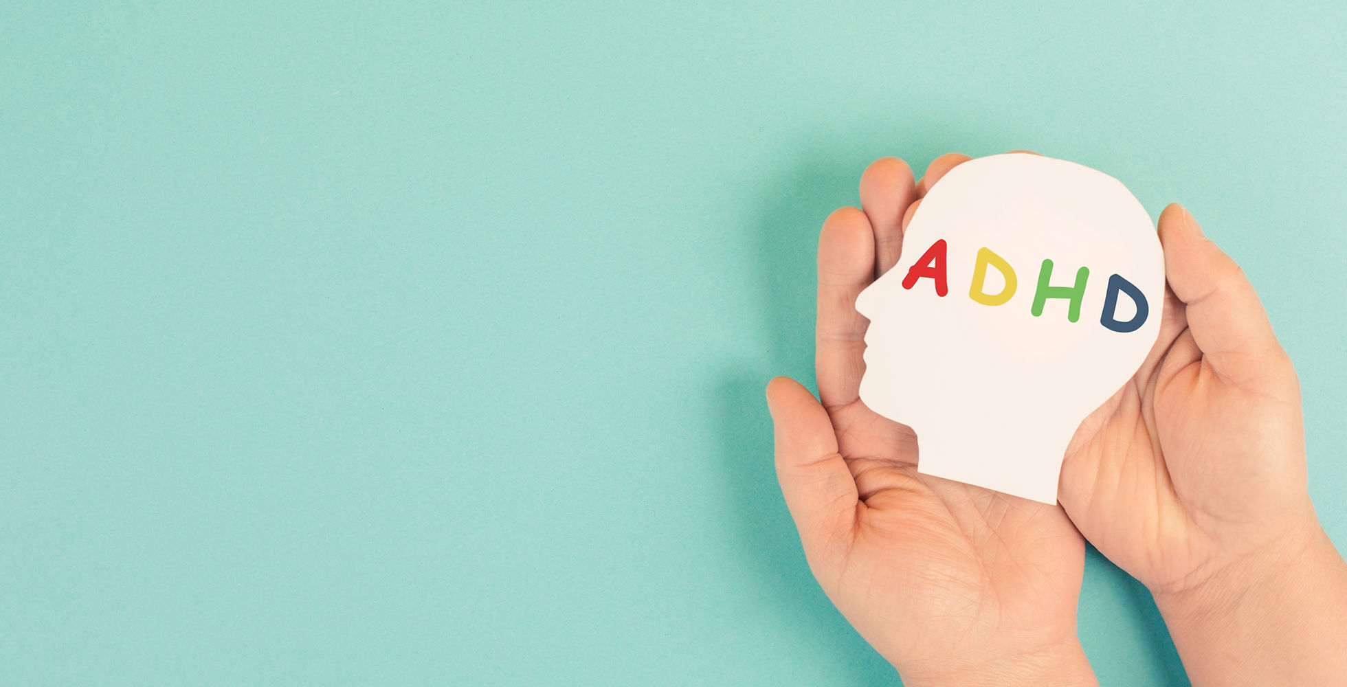 The word ADHD in rainbow letters on a cutout of a head, held in a person' palms.