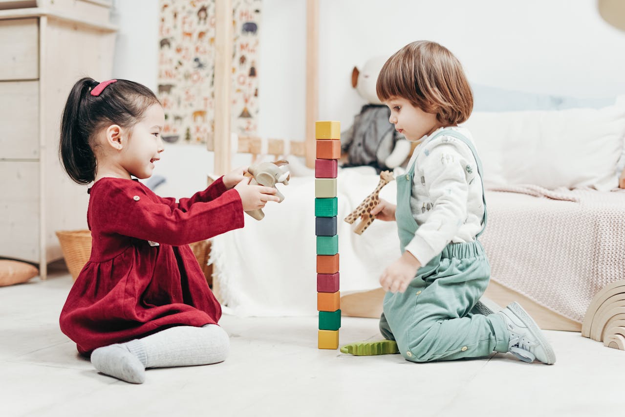 boy-in-white-long-sleeve-shirt-and-green-pants-sitting-on-floor-beside-girl-in-red